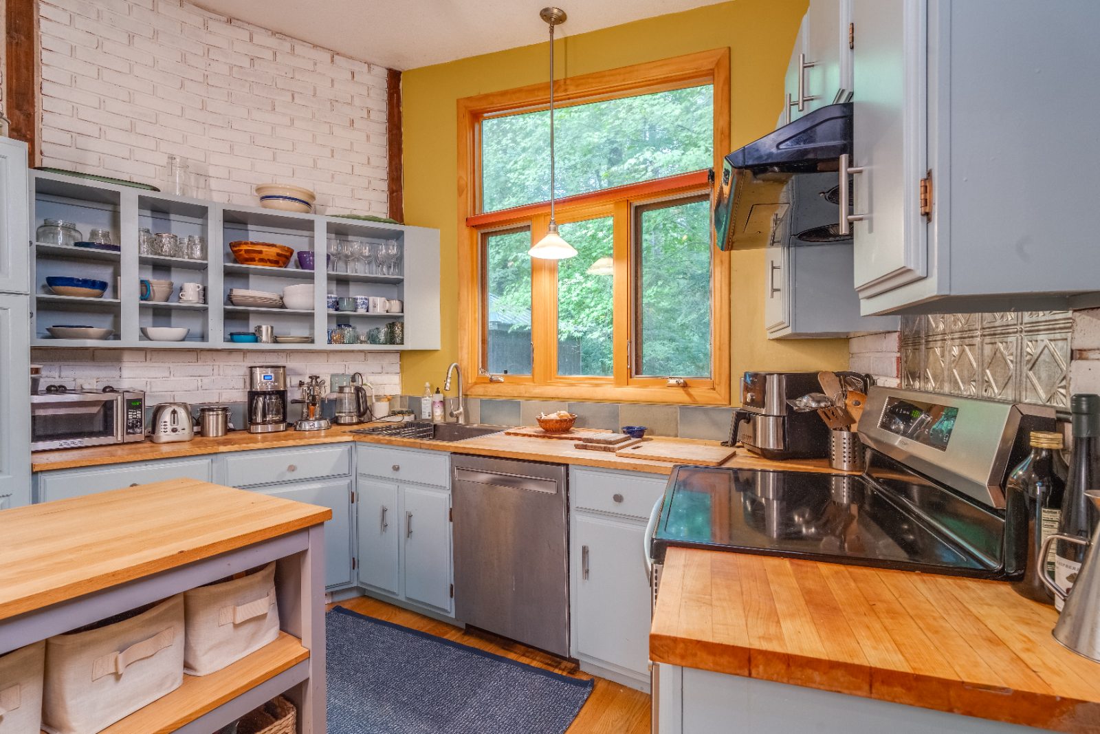 Kitchen with butcher-block counters, open shelving and a large window onto the woods
